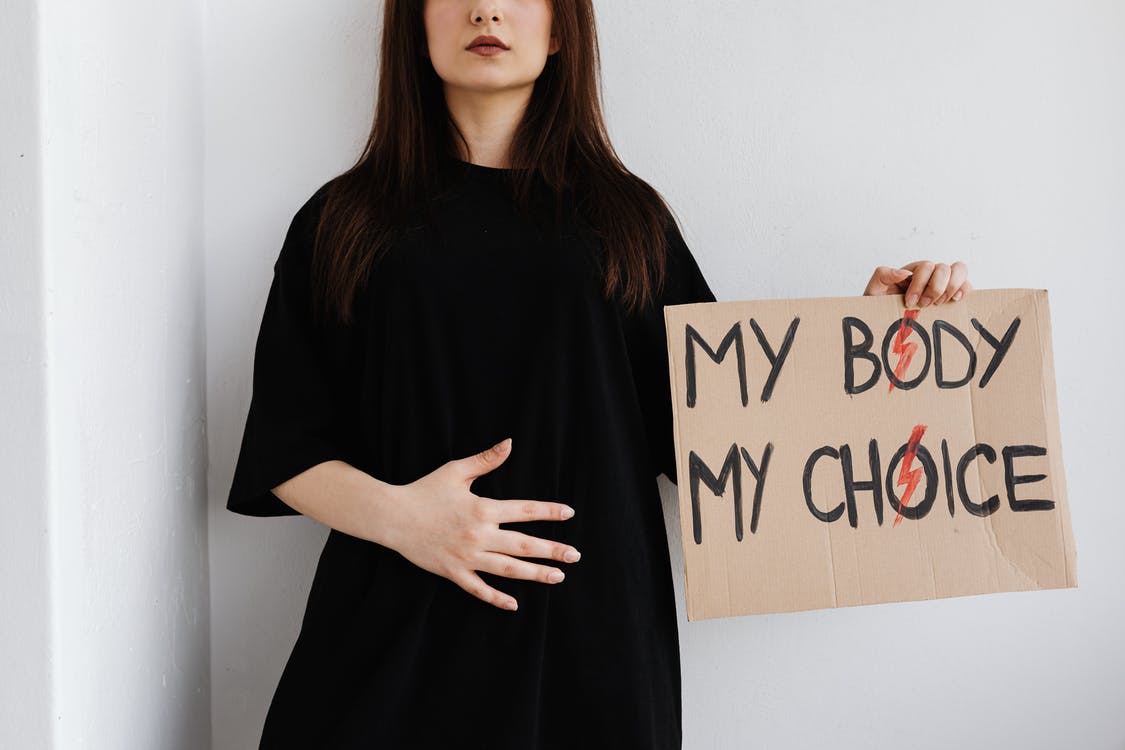 An image of a person with an oversized maternity dress, with a sign saying my body my choice